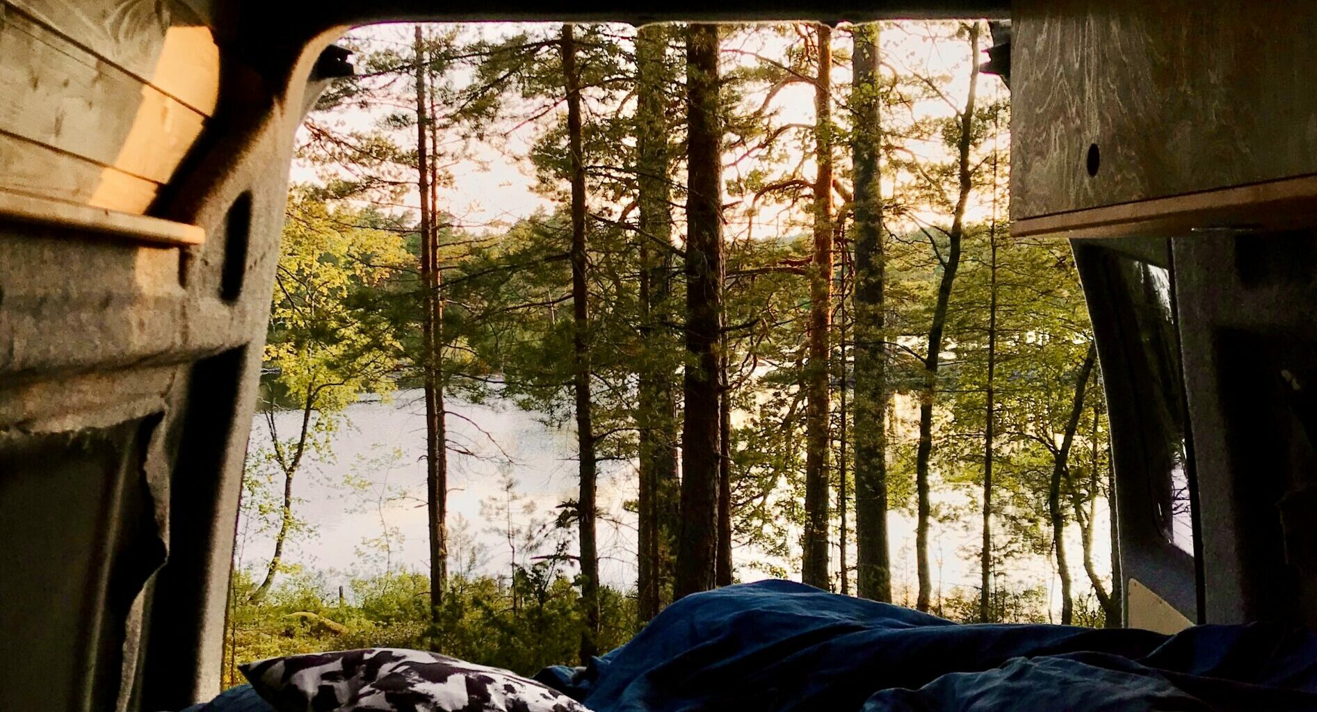 view from inside a camper van outside; with green trees and a lake in the background