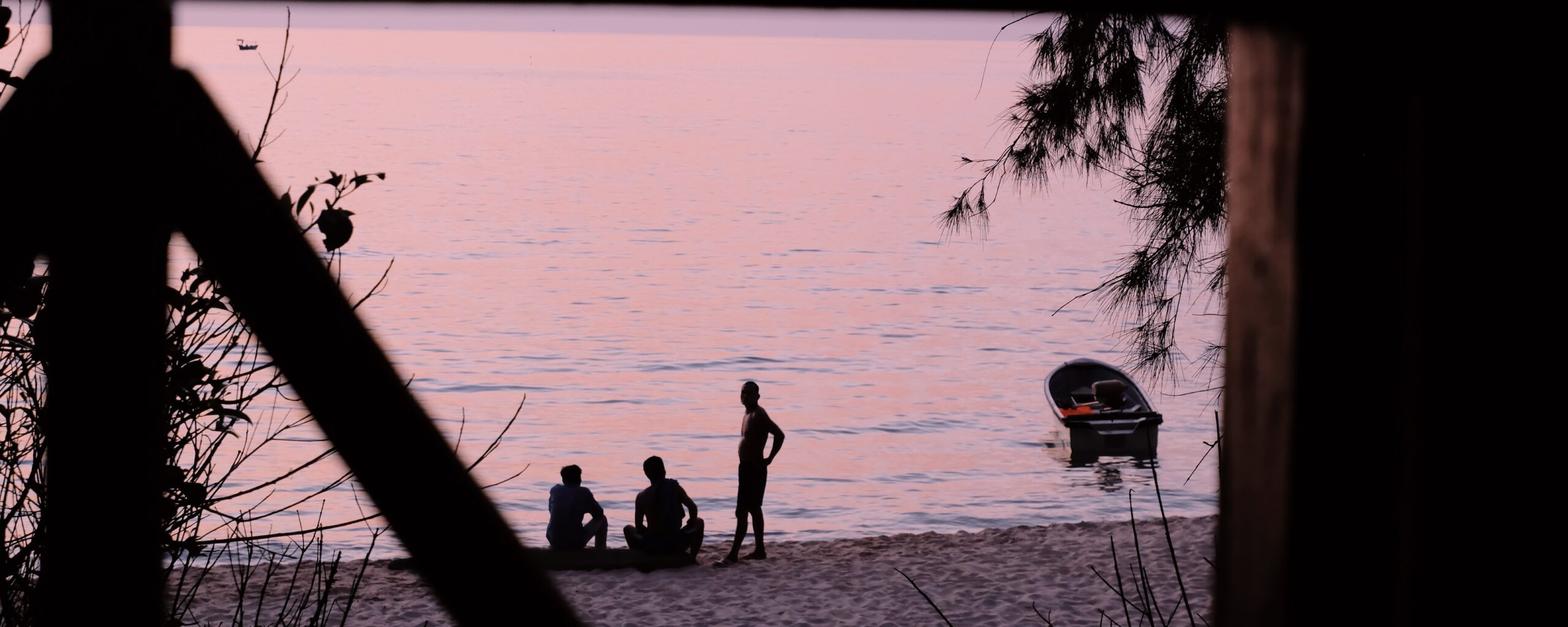 silhouettes of three men and a boat before a pink ocean with trees