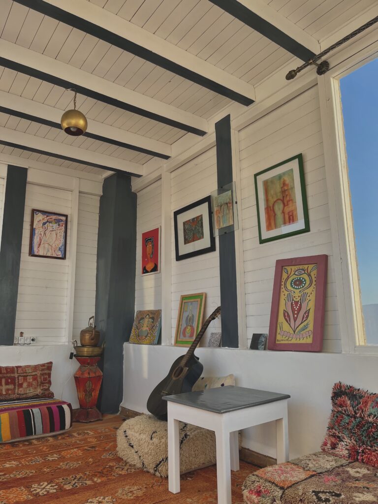 cozy room with pictures on the wall and a guitar sitting on a pouf 